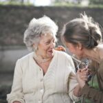 Home Joyful interaction between an elderly woman and her granddaughter in a sunny outdoor setting.