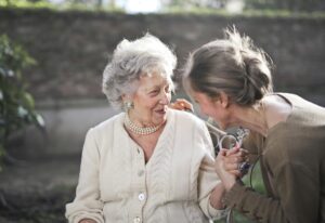Home Joyful interaction between an elderly woman and her granddaughter in a sunny outdoor setting.